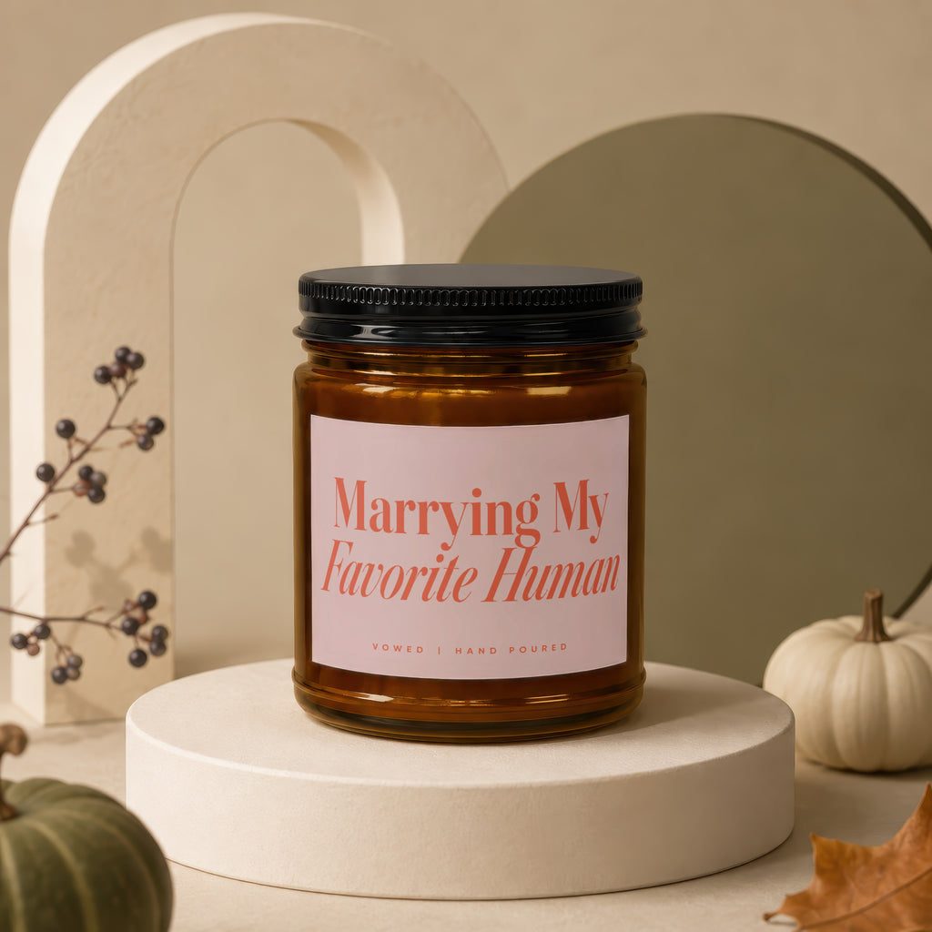 Amber jar candle with pink label reading "Marrying My Favorite Human" and "Vowed | Hand Poured".