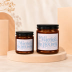 Two amber glass candles with black lids, labels read "Married the plot twist."