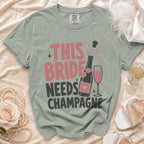T-shirt with "THIS BRIDE NEEDS CHAMPAGNE" graphic and champagne bottle.