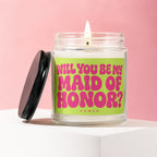 Glass candle with lit wick and bright pink text asking "Will You Be My Maid of Honor?".