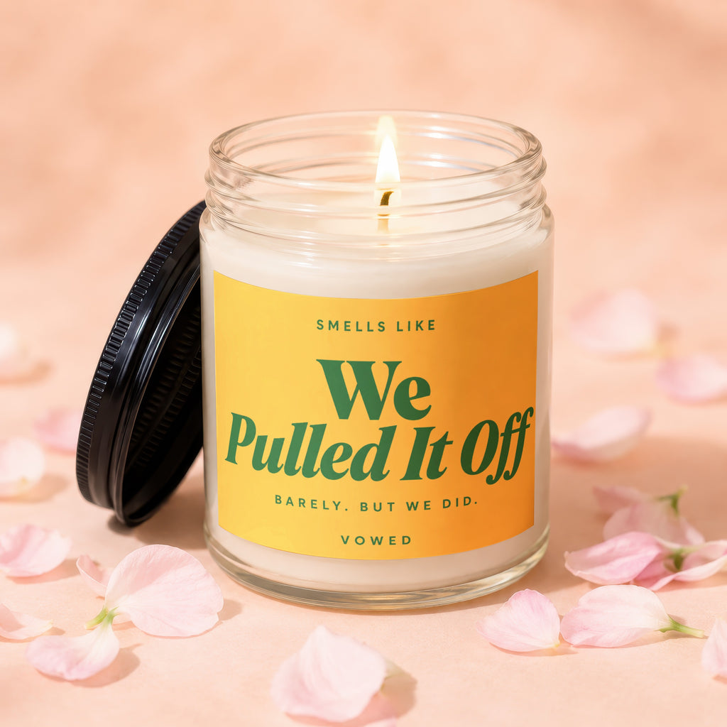 Scented candle in a glass jar with a light flame and a yellow label that says "We Pulled It Off"