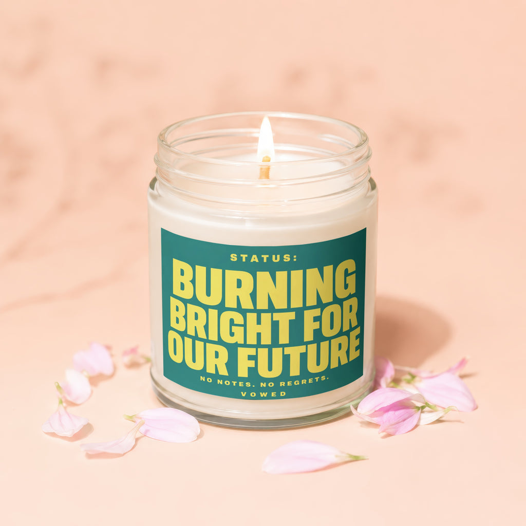 Glass candle with lit wick and text "STATUS: BURNING BRIGHT FOR OUR FUTURE".