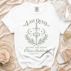 White t-shirt featuring green fantasy-themed text that reads Last Quest Before the Dress and Olivia's Bachelorette Asheville, NC.