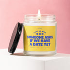 Lit candle with yellow label reading "Light me when someone asks if we have a date yet."