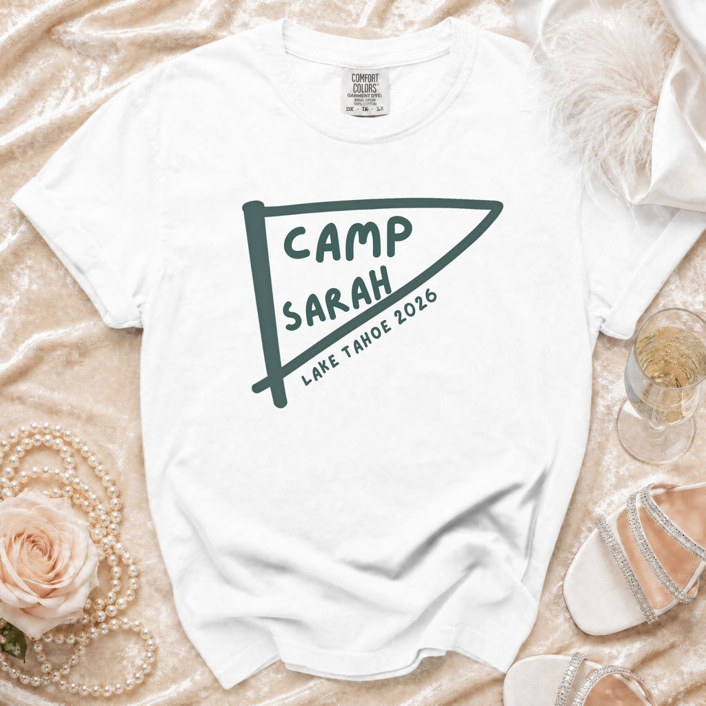 White t-shirt with "Camp Sarah Lake Tahoe 2026" text on a pennant graphic.