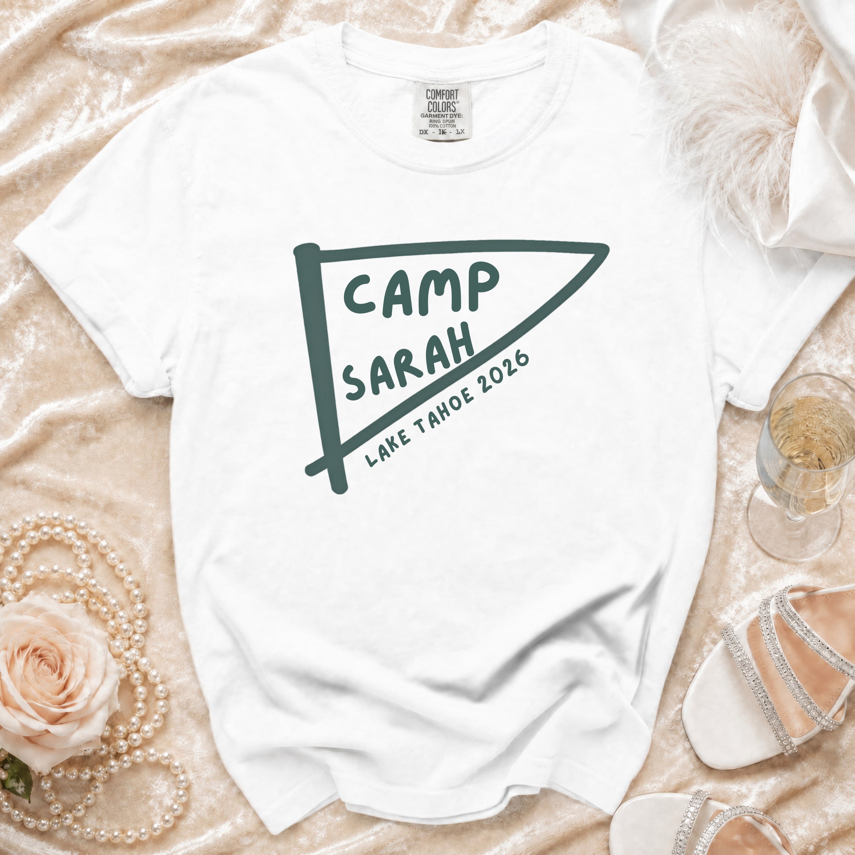 White t-shirt with "Camp Sarah Lake Tahoe 2026" text on a pennant graphic.