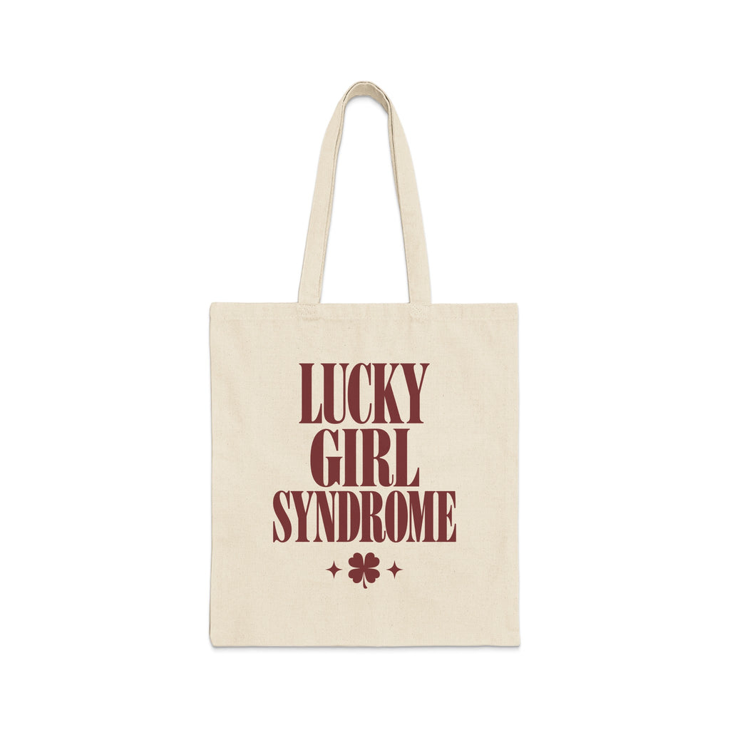 A natural canvas tote bag printed with maroon text reading Lucky Girl Syndrome above a four-leaf clover.