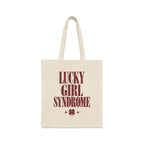 A natural canvas tote bag printed with maroon text reading Lucky Girl Syndrome above a four-leaf clover.