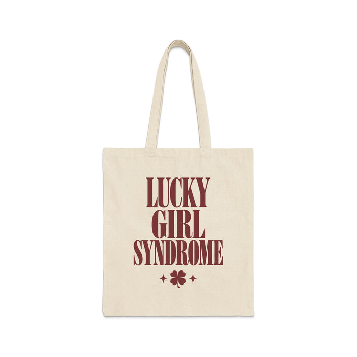 A natural canvas tote bag printed with maroon text reading Lucky Girl Syndrome above a four-leaf clover.