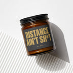 Amber jar candle with black lid and label reading "DISTANCE AIN'T SH*T"