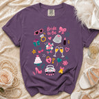 Purple t-shirt with "Bride to Be" and wedding icons, including a cake, car, and champagne.