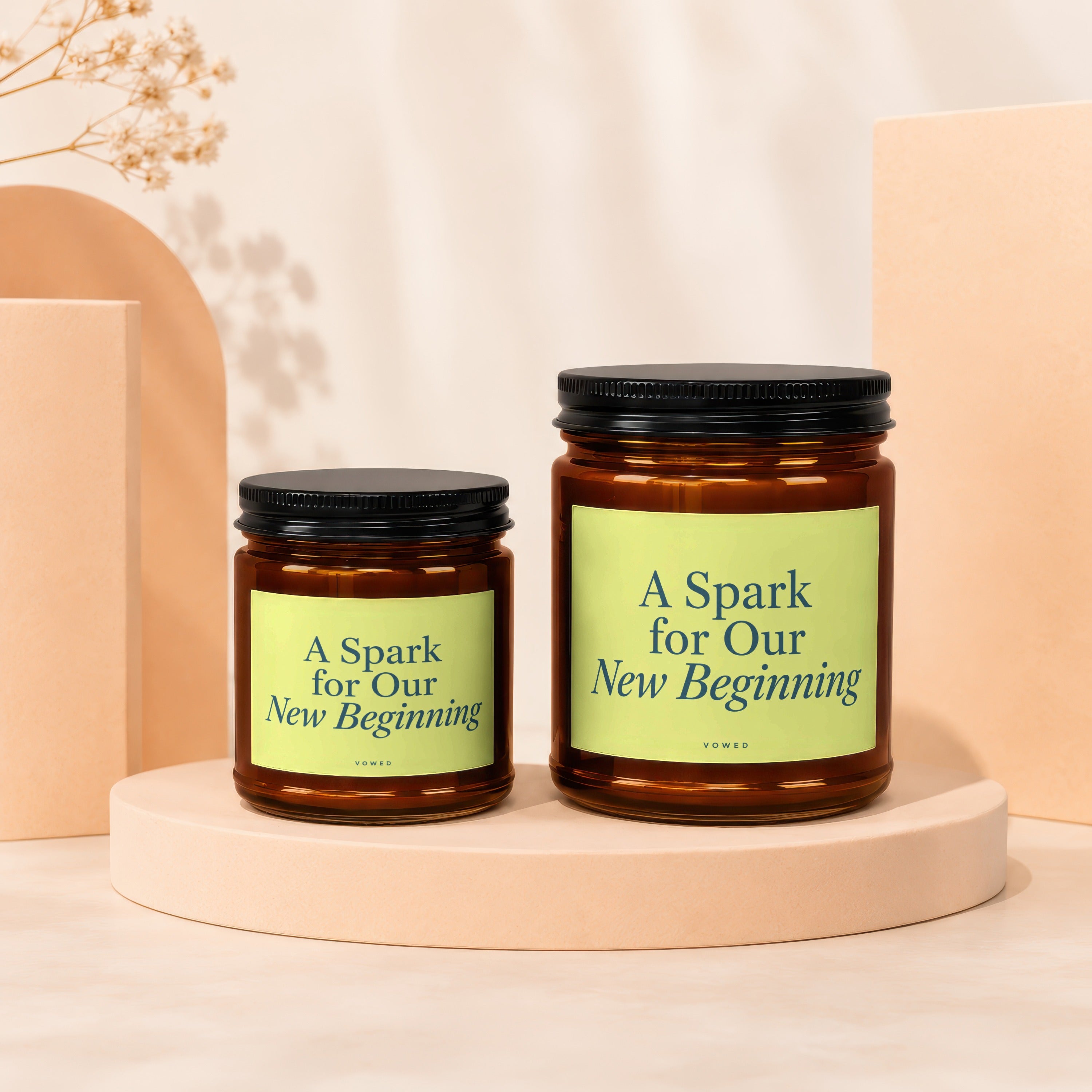 Two glass candles with "A Spark for Our New Beginning" text displayed on pastel pedestals.