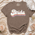 Brown t-shirt with "Bride" in colorful retro text, styled with pearls and heels.