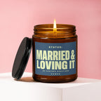 Amber glass candle with lit wick. Label reads "STATUS: MARRIED & LOVING IT".