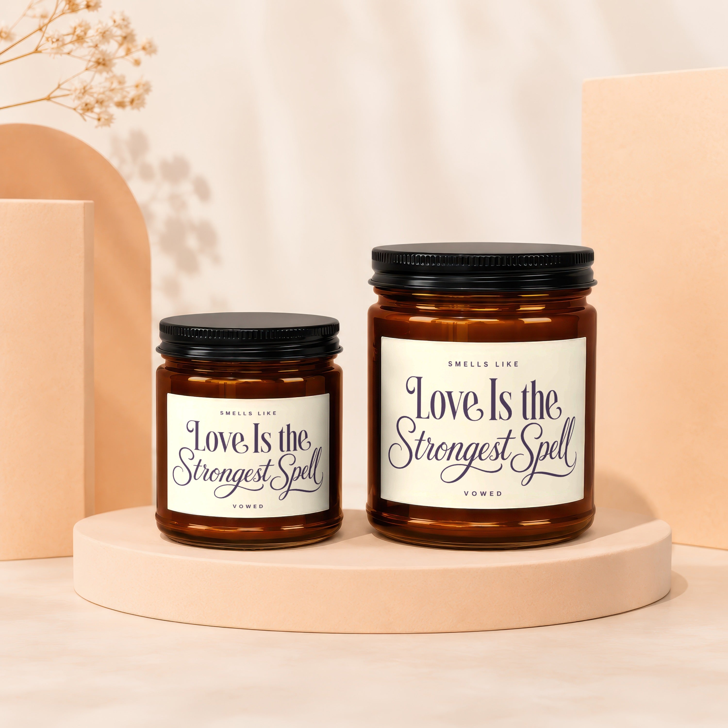 Two amber glass candles with black lids, labeled "Love Is the Strongest Spell."