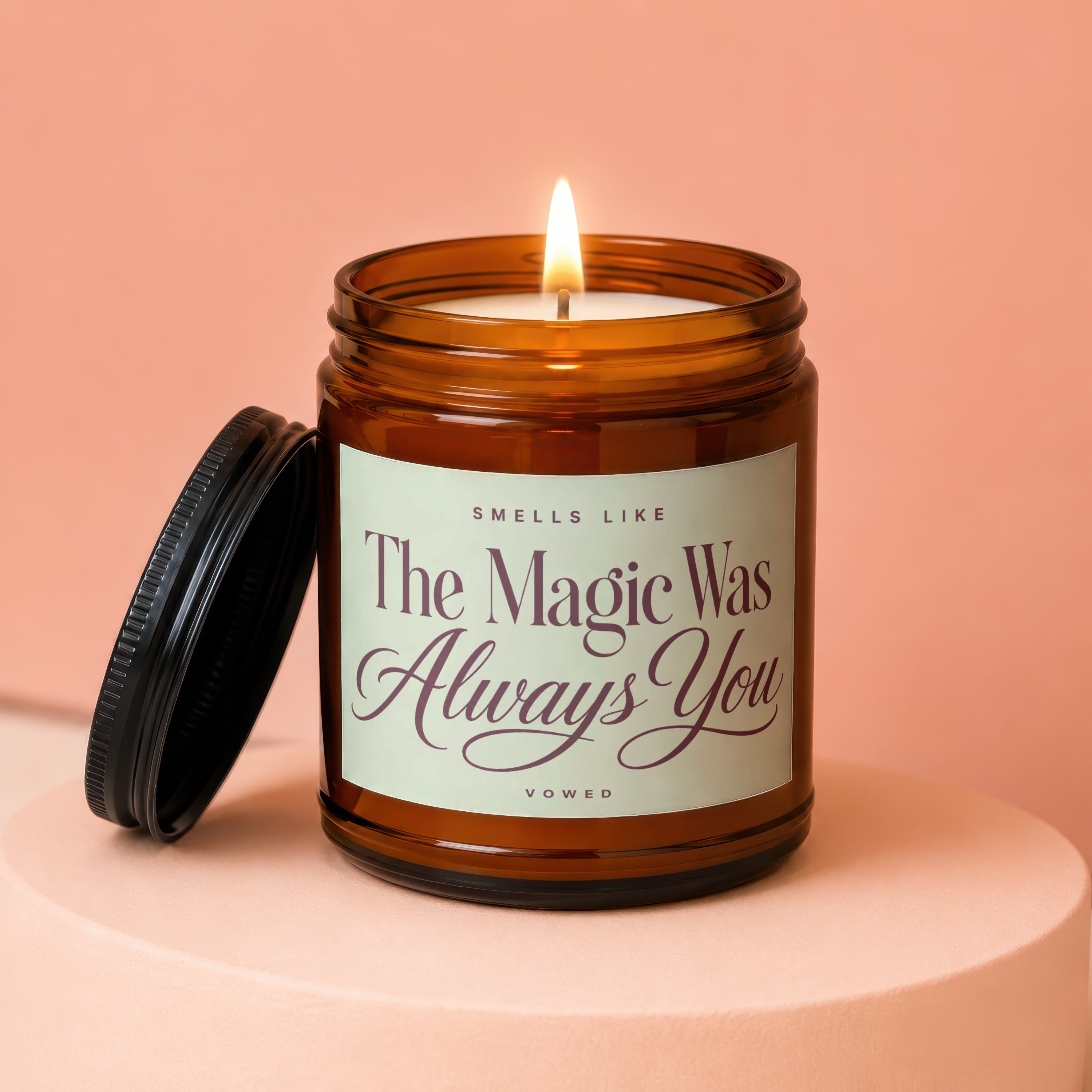 A lit amber jar candle with lid beside it, reading "Smells Like The Magic Was Always You".
