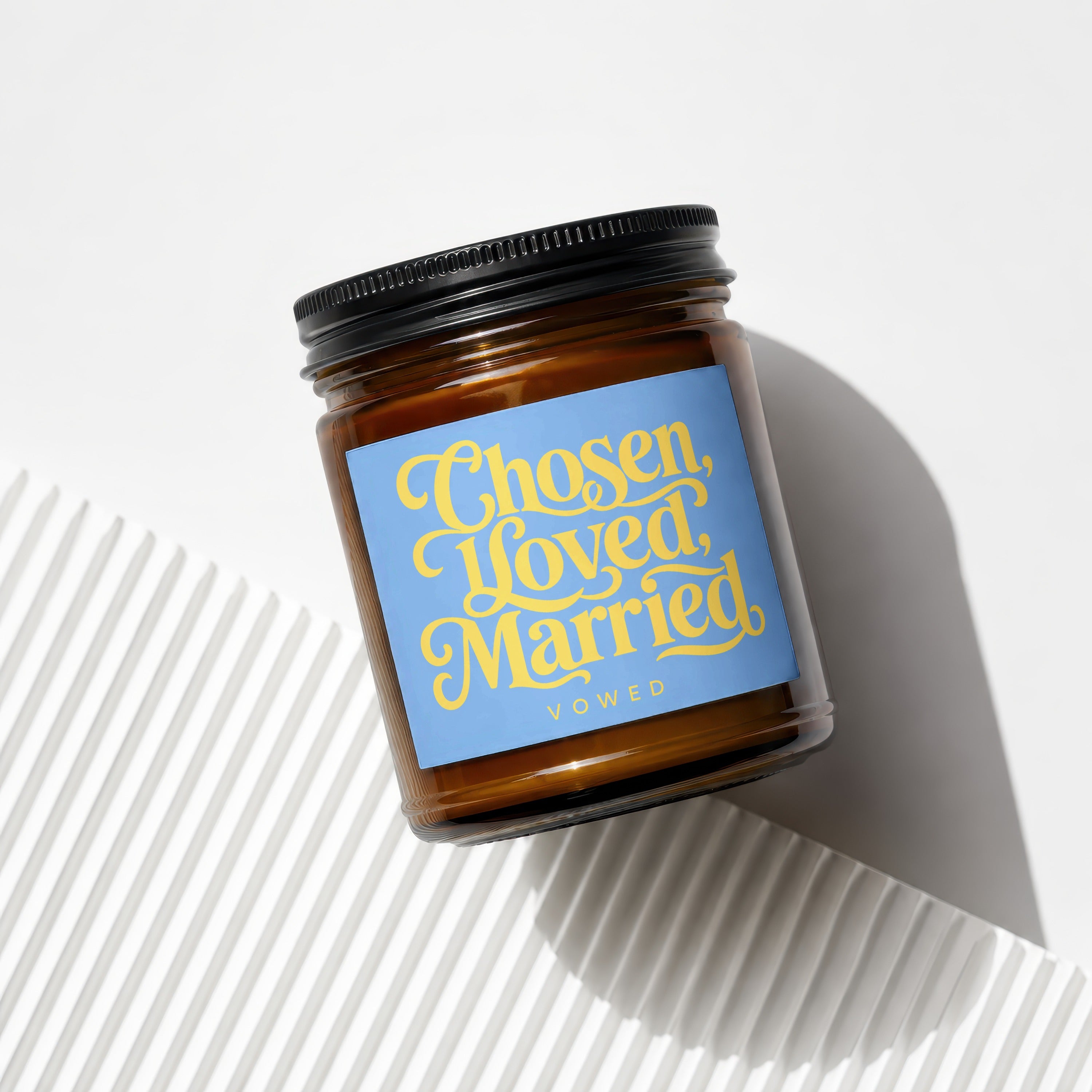 Amber jar candle with blue label reading "Chosen, Loved, Married. VOWED."