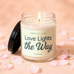 Lit candle in glass jar with black lid, text reads "Smells Like Love Lights the Way Vowed".