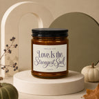 Amber jar candle with black lid reading "Love Is the Strongest Spell"