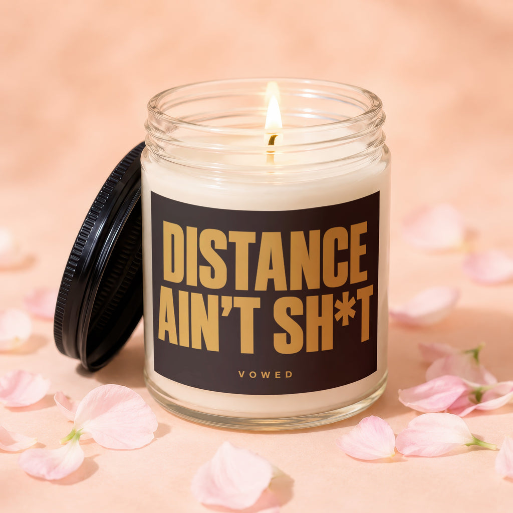 Jar candle with lit wick and label "DISTANCE AIN'T SH*T VOWED".