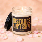 Jar candle with lit wick and label "DISTANCE AIN'T SH*T VOWED".