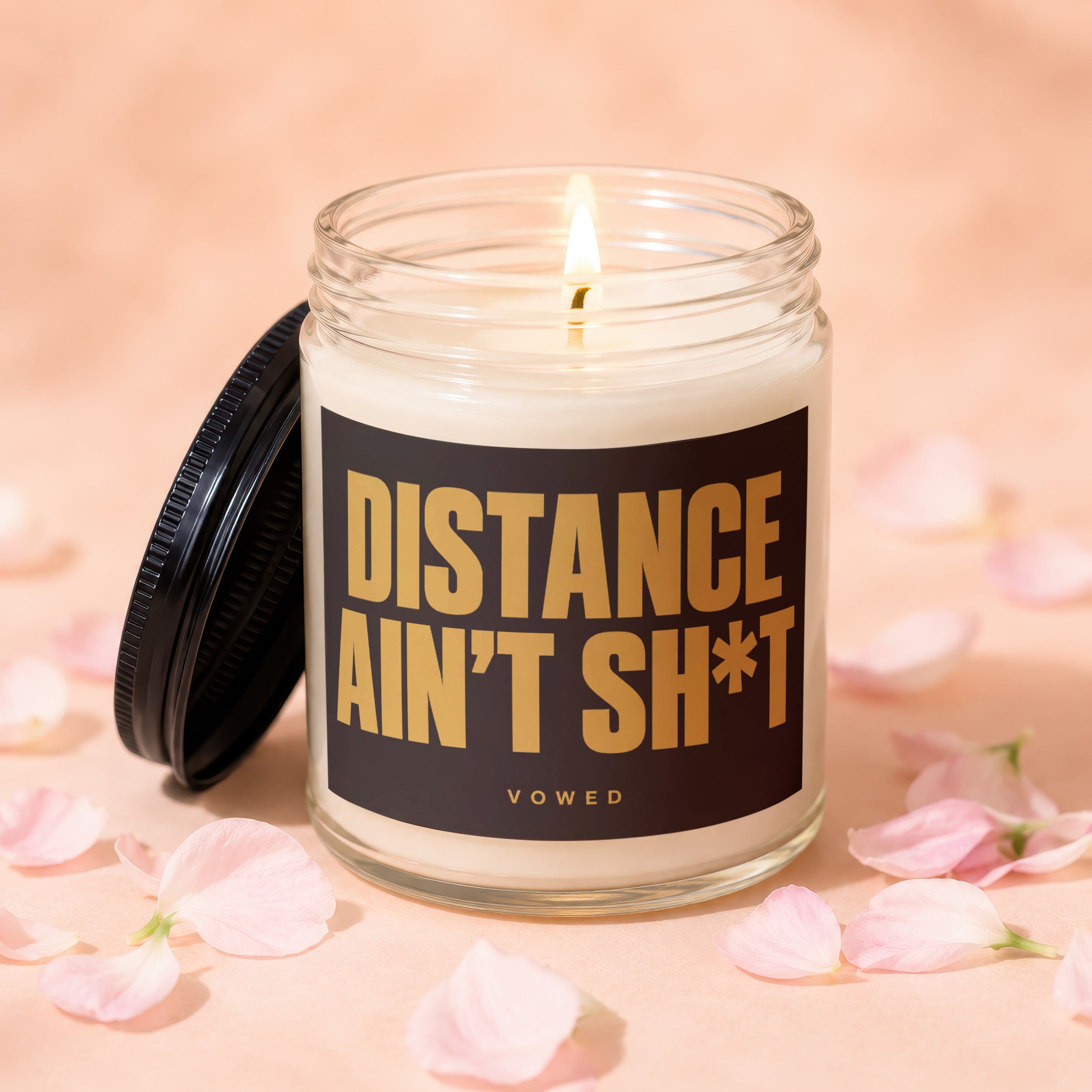 Jar candle with lit wick and label "DISTANCE AIN'T SH*T VOWED".