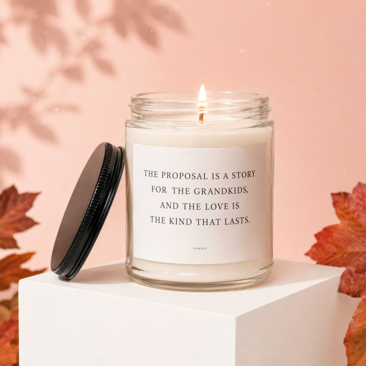 Glass jar candle with lit wick, lid off, and text "The proposal is a story for the grandkids, and the love is the kind that lasts."