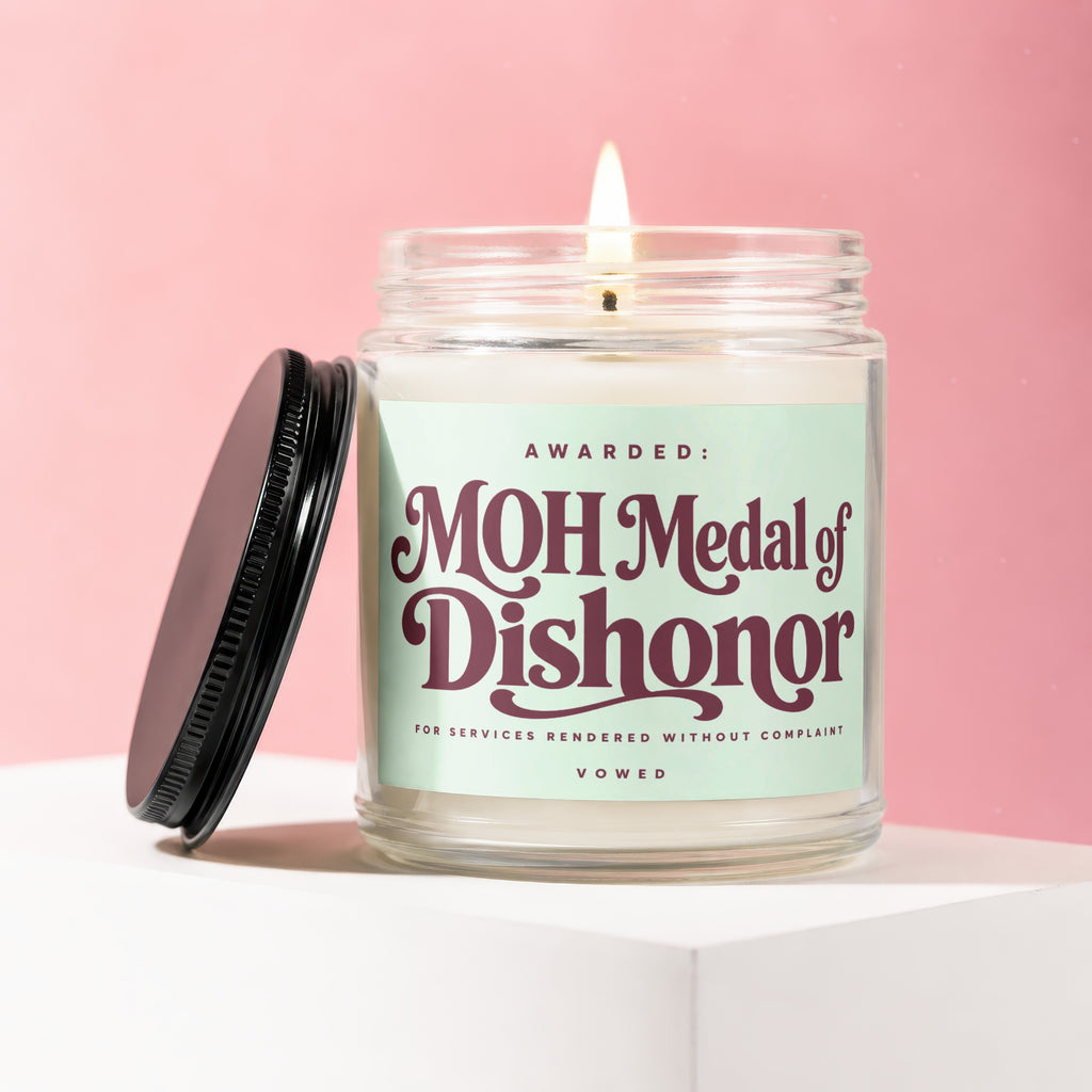 Candle with "MOH Medal of Dishonor" label against pink background.