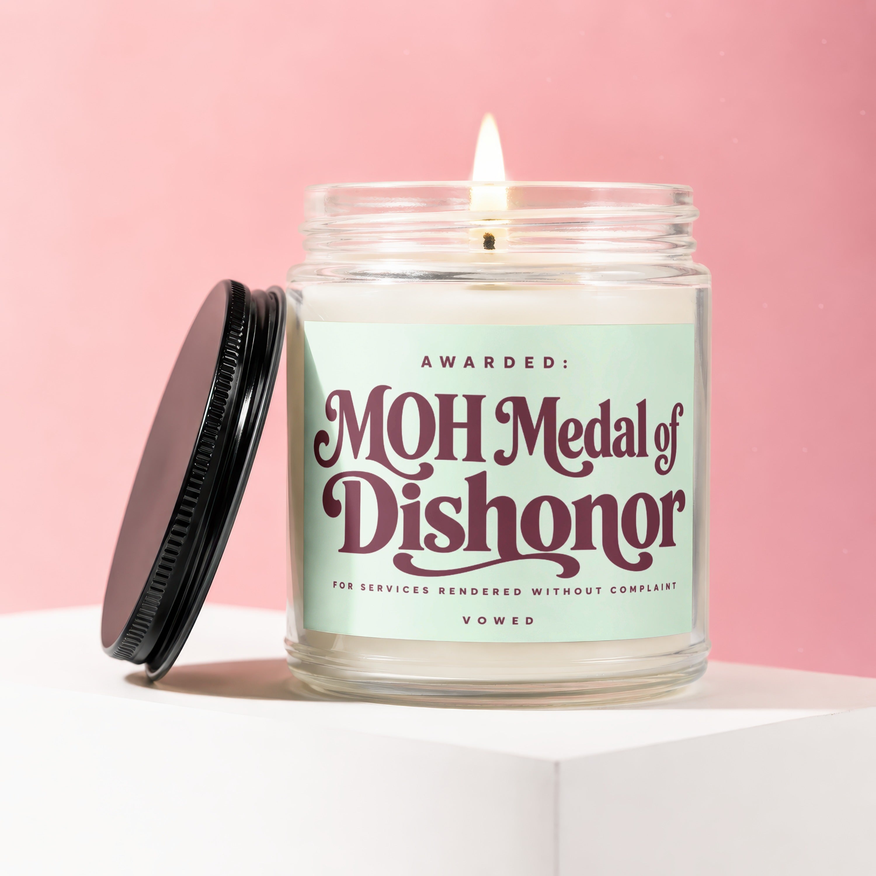 Candle with "MOH Medal of Dishonor" label against pink background.