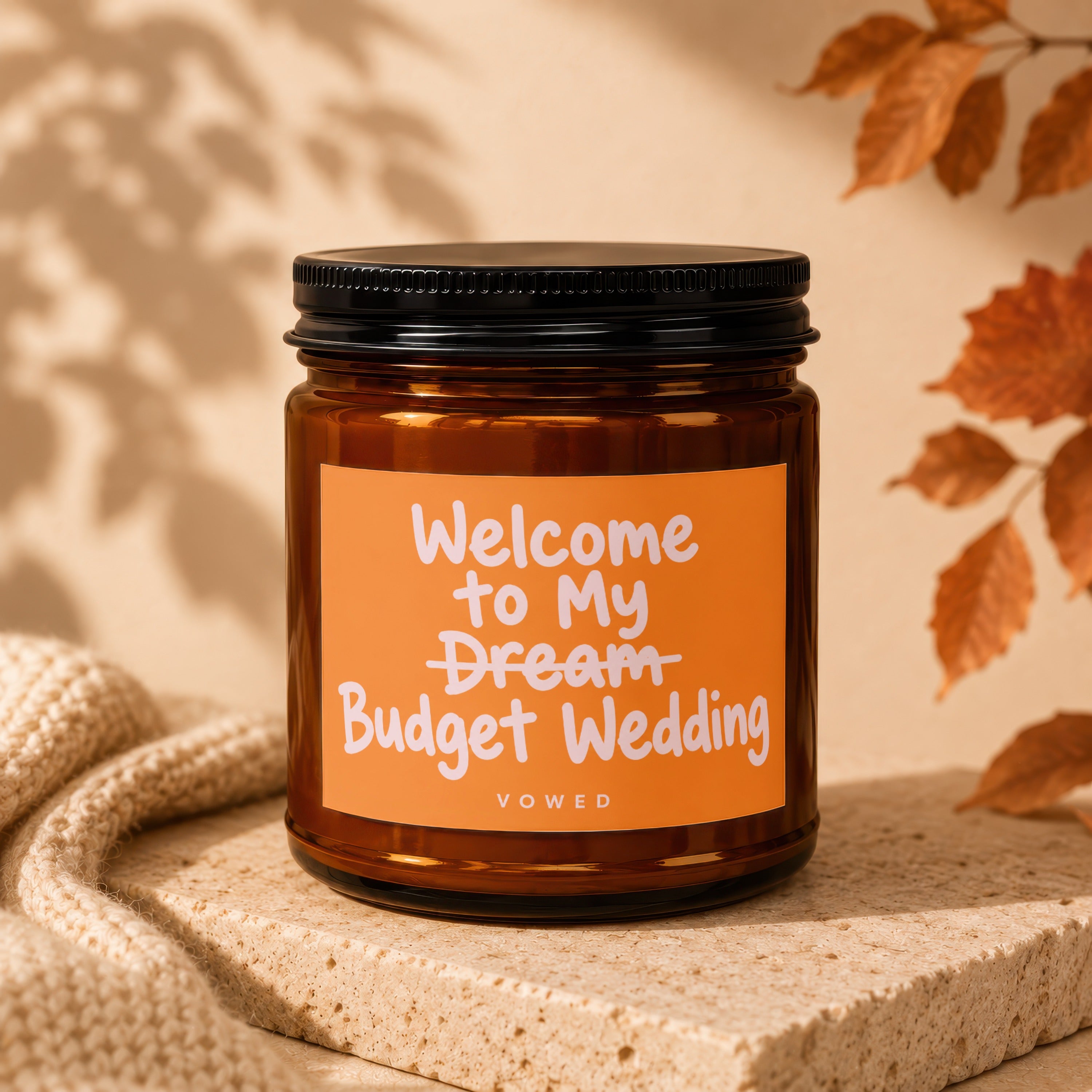 Amber candle with black lid reads "Welcome to My Budget Wedding" by Vowed.