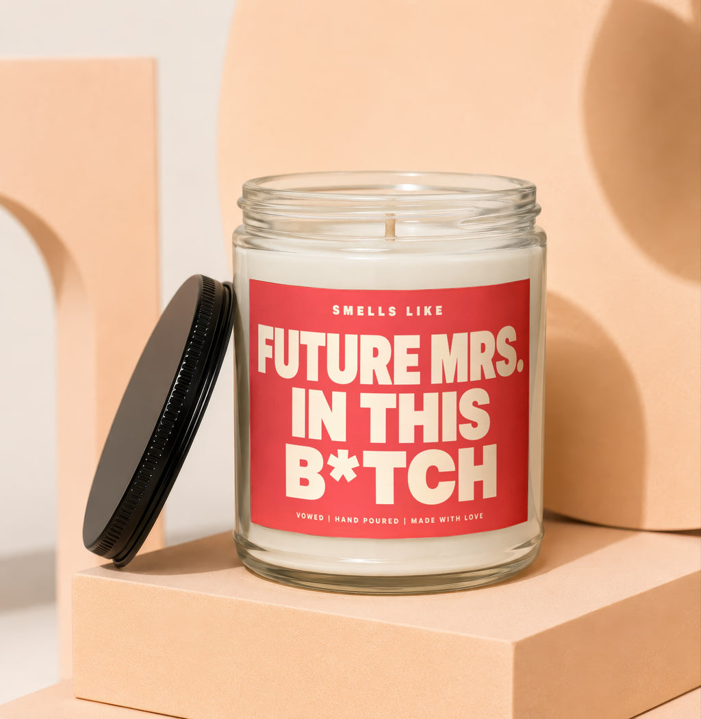 Candle with red label that reads "Smells Like Future Mrs. In This B*tch".