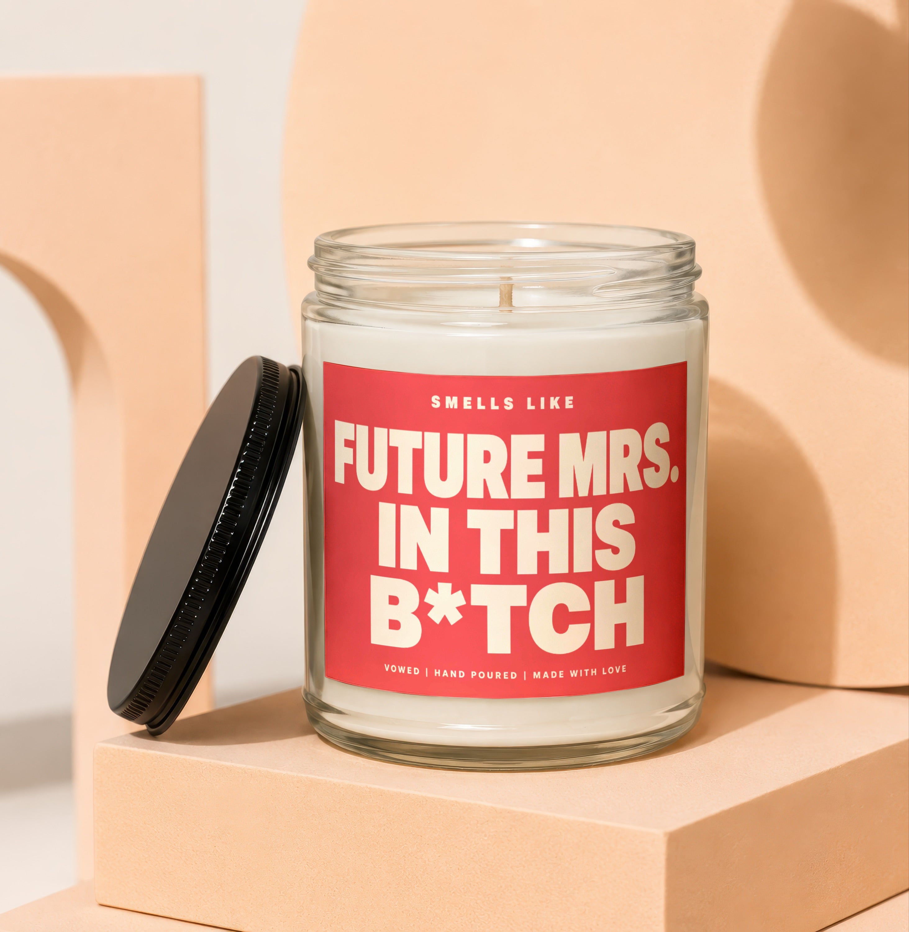 Candle with red label that reads "Smells Like Future Mrs. In This B*tch".