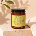 Amber glass candle with "We Chose This VOWED" text on yellow label.