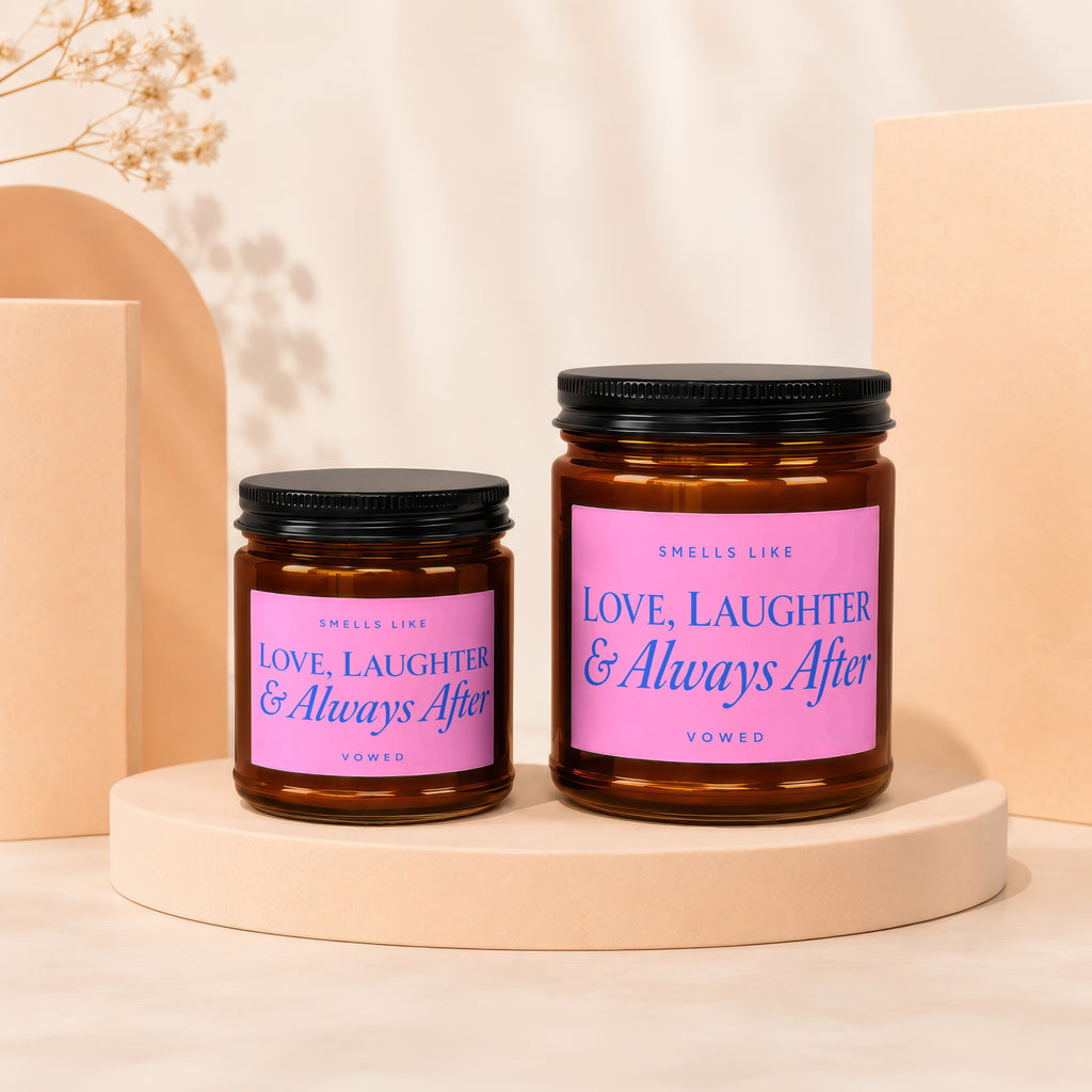 Two amber glass candles with pink labels reading "Smells Like Love, Laughter & Always After Vowed".
