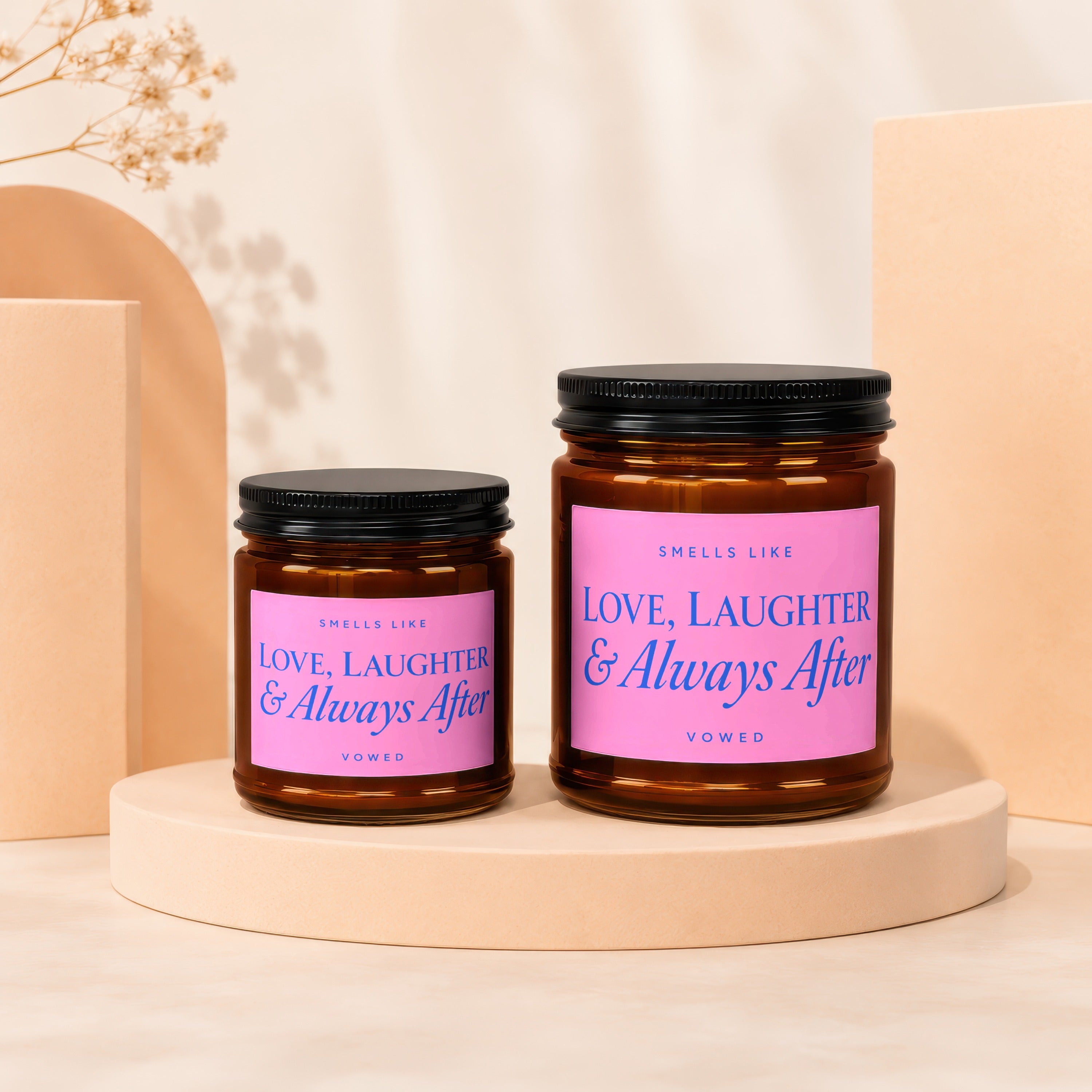 Two amber glass candles with pink labels reading "Smells Like Love, Laughter & Always After Vowed".