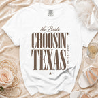 White t-shirt with brown text reading the Bride CHOOSIN TEXAS AUSTIN, TX, 2027 laid on a velvet background.