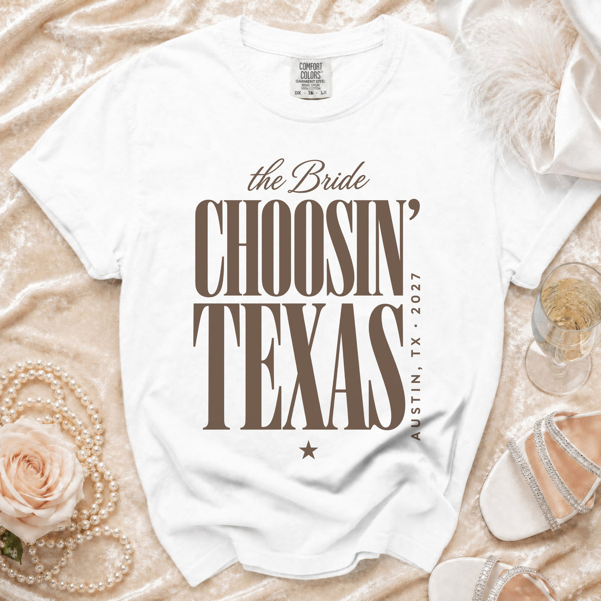 White t-shirt with brown text reading the Bride CHOOSIN TEXAS AUSTIN, TX, 2027 laid on a velvet background.
