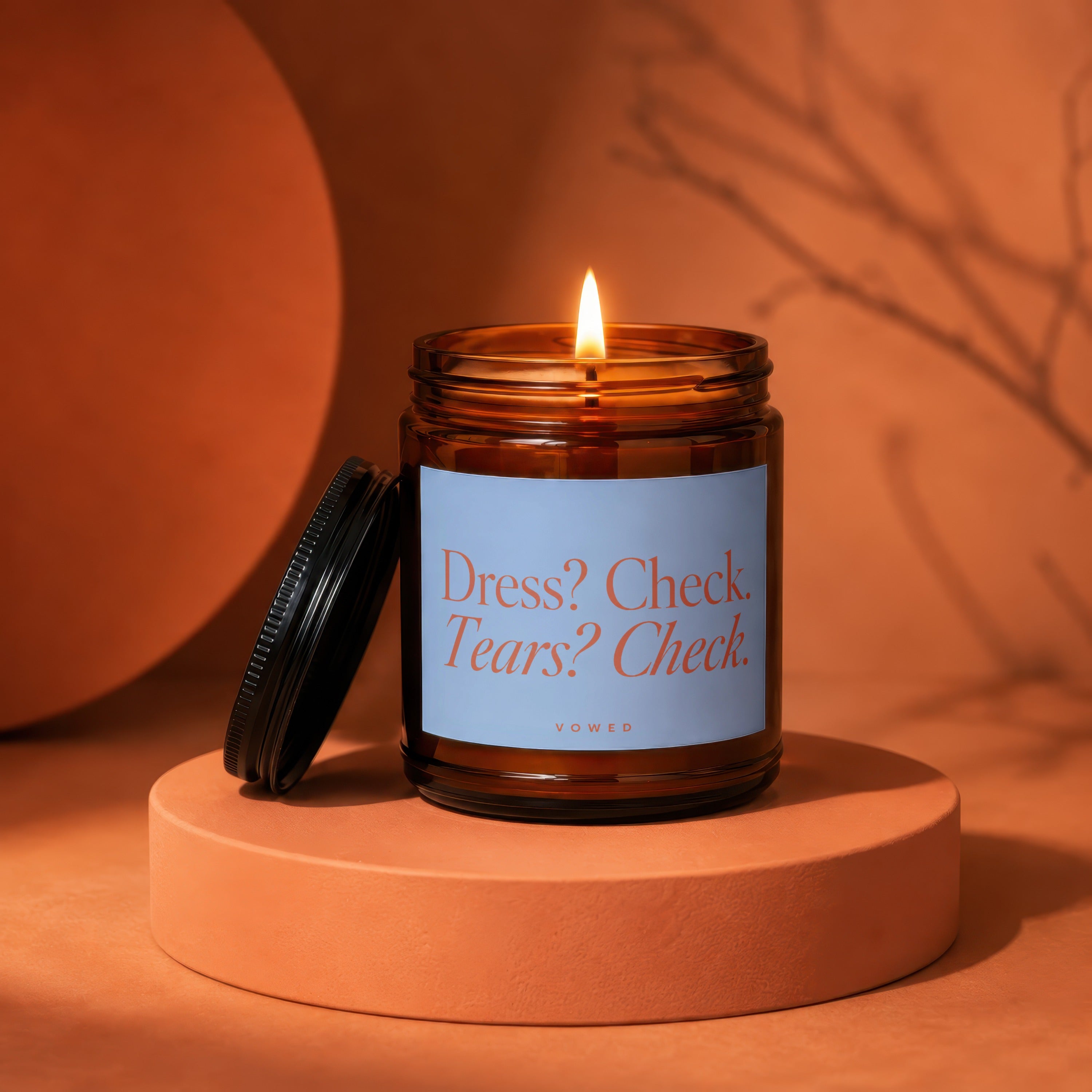 Burning amber glass candle with a light blue label reading "Dress? Check. Tears? Check."