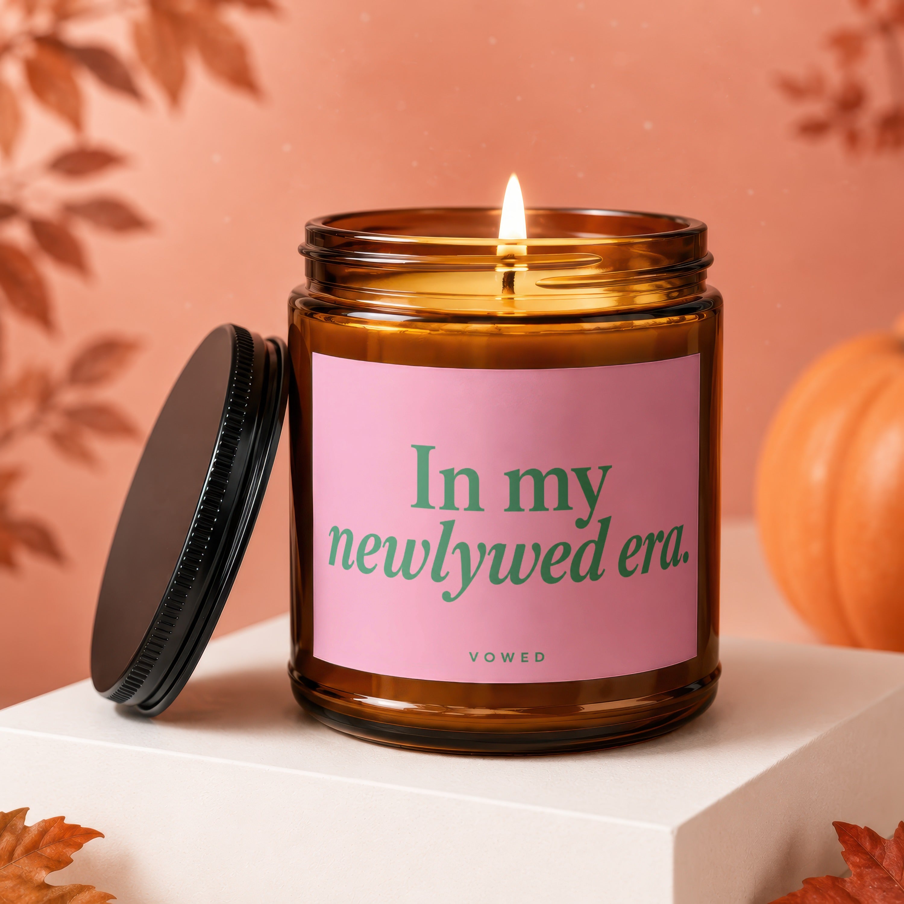 Amber candle with lit wick and pink label reading "In my newlywed era."