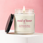 Glass candle with lit wick and black lid, reads "maid of honor noun. the friend who said yes before I finished asking."