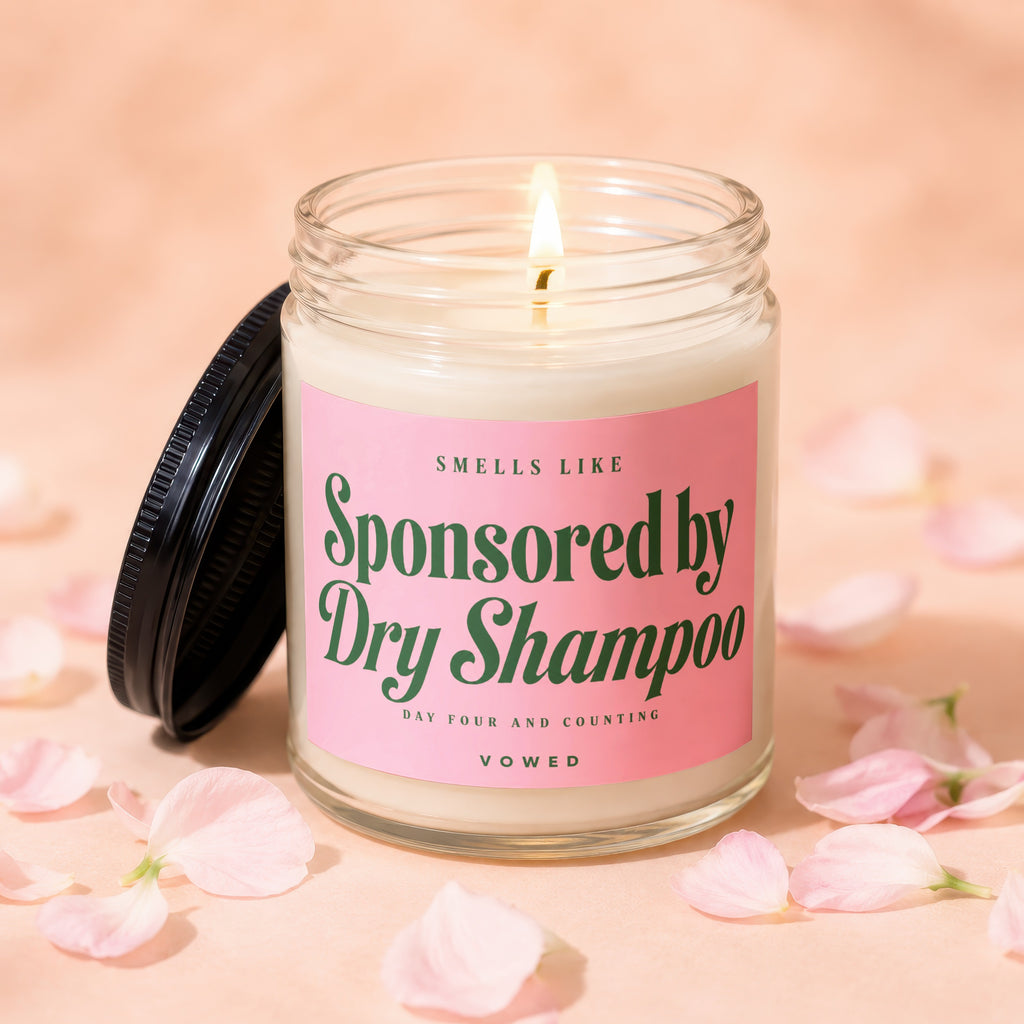 Lit candle in jar with pink label that says "Smells Like Sponsored by Dry Shampoo".