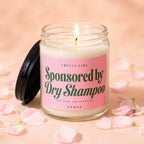 Lit candle in jar with pink label that says "Smells Like Sponsored by Dry Shampoo".