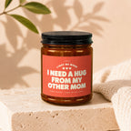 Candle with text "I Need A Hug From My Other Mom" on coral label.