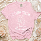 Pink t-shirt with "Reckless in Texas Austin, TX Summer 2026 Olivia's Bach" text.