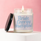 Lit candle in glass jar with black lid, labeled "Bride Energy Multiplied VOWED".