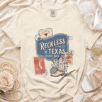 Cream t-shirt with "Reckless in Texas" and disco boot graphic.