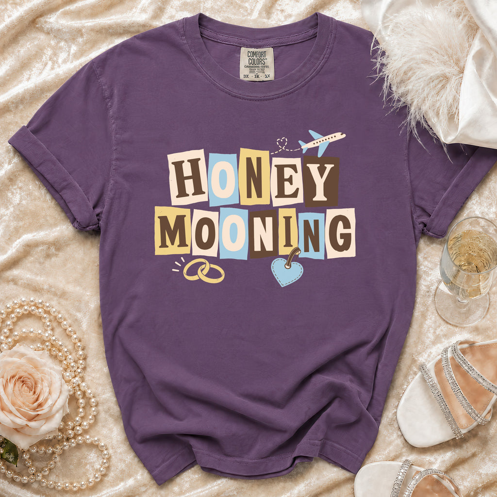 Purple t-shirt with "Honeymooning" text, wedding rings, and airplane graphic.