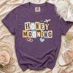 Purple t-shirt with "Honeymooning" text, wedding rings, and airplane graphic.
