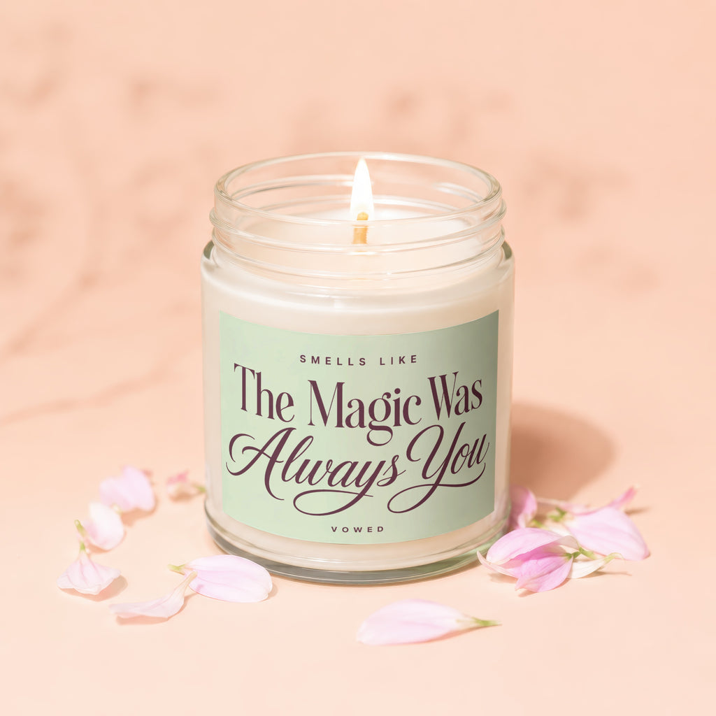 Lit candle with "The Magic Was Always You" text, surrounded by pink petals.