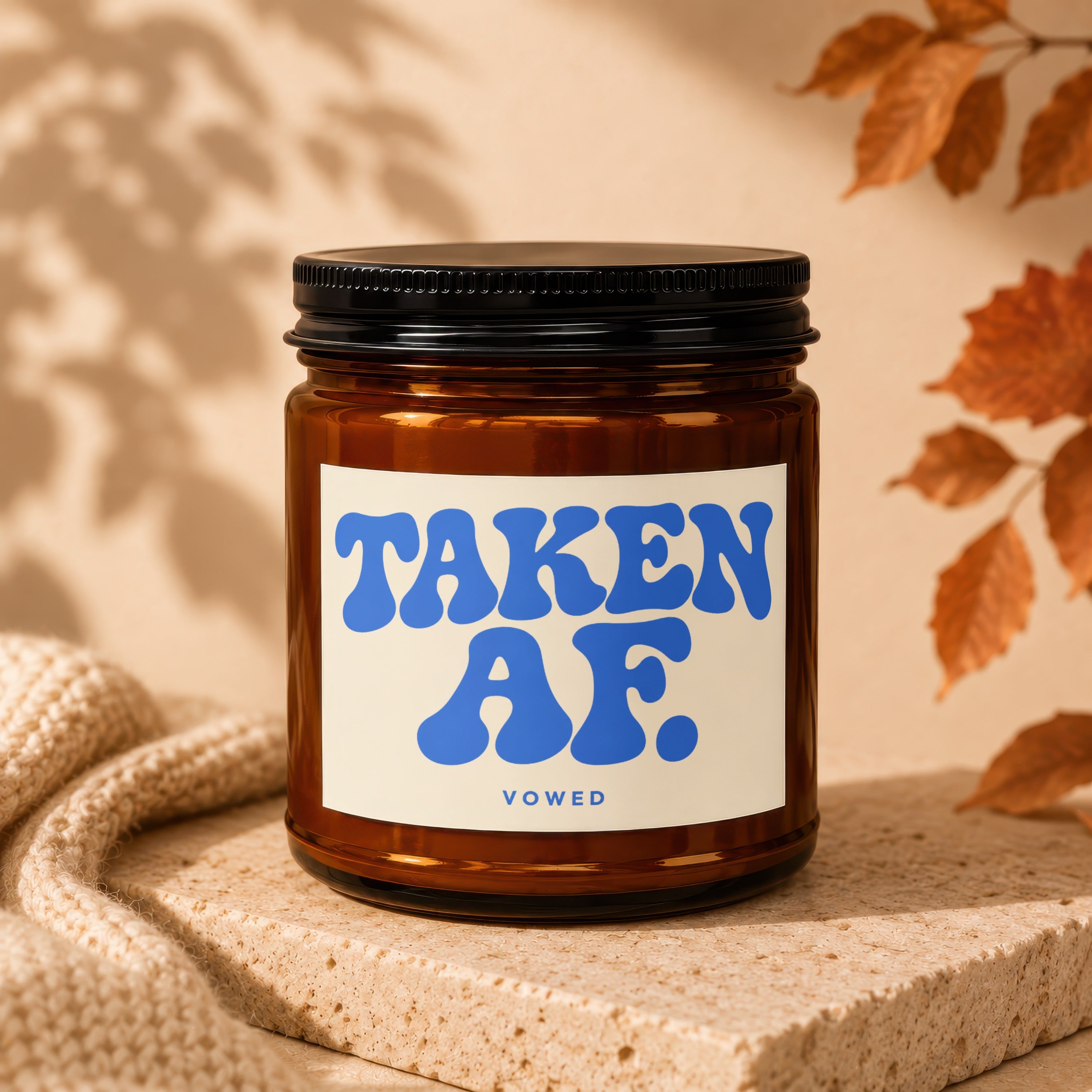 Amber glass candle with "TAKEN AF" and "VOWED" text on a cream label.